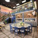 ‘Mystery Hotel Theme’ Set Plates of the Big Brother House for season 27 of the CBS Original Series BIG BROTHER, scheduled to air on the CBS Television Network.  Pictured: Rooftop Garden Kitchen: The kitchen and dining area mimic a rooftop garden with ivy-covered walls, sunset skies and a 10-foot round garden party table under string lights. Photo: Matthew Taplinger ©2025 CBS Broadcasting, Inc. All Rights Reserved.